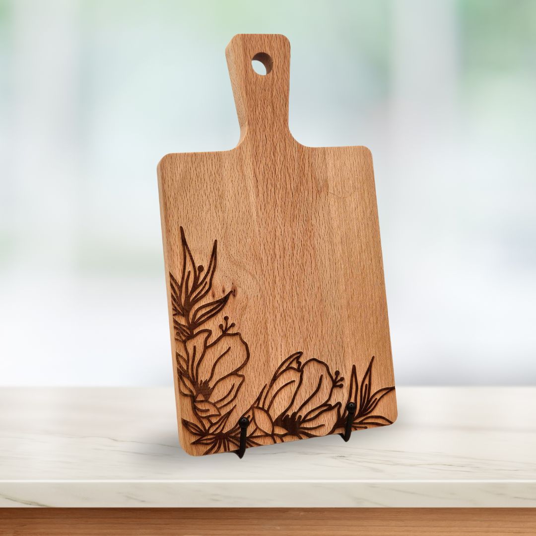 A light wood serving board with laser-engraved flowers along the bottom and left edges.