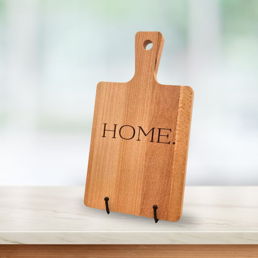 A light wood serving board with the word "HOME." laser-engraved in the middle of the board.