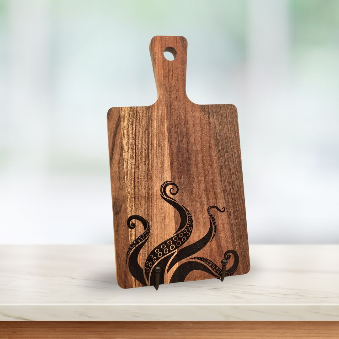 A dark wood serving board with laser-engraved octopus / Kraken tentacles rising from the bottom.