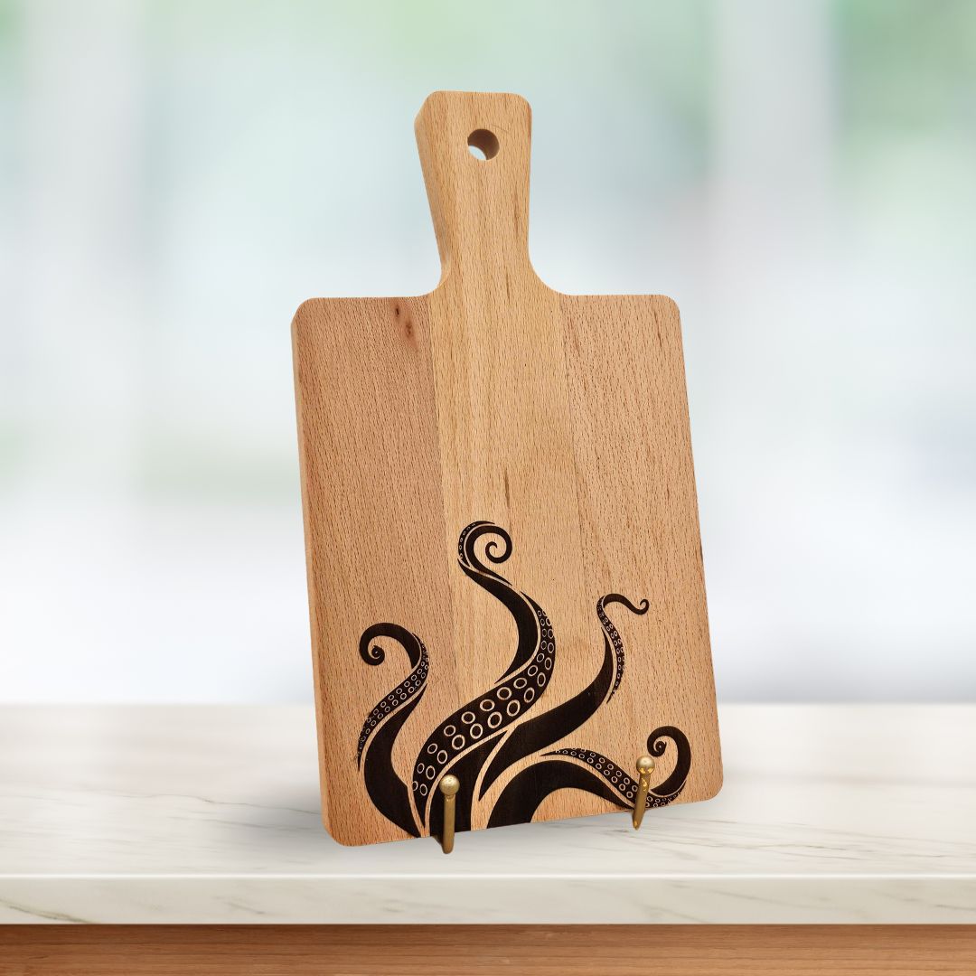 A light wood serving board with laser-engraved octopus / Kraken tentacles rising from the bottom.